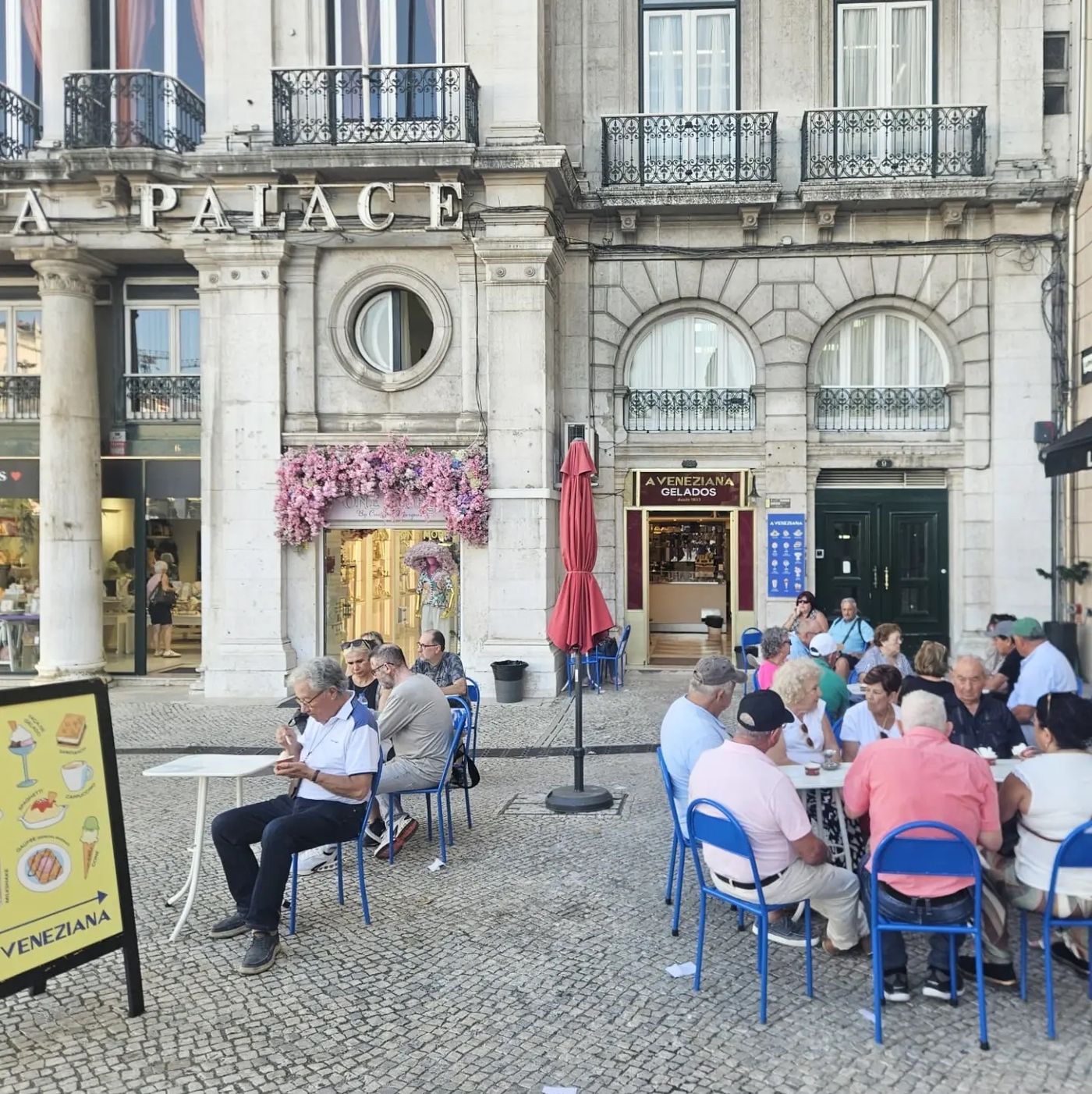 The A Veneziana Gelados shopfront on Praca dos Restauradores, its gold sign reading desde 1933, with customers at blue chairs on the terrace outside