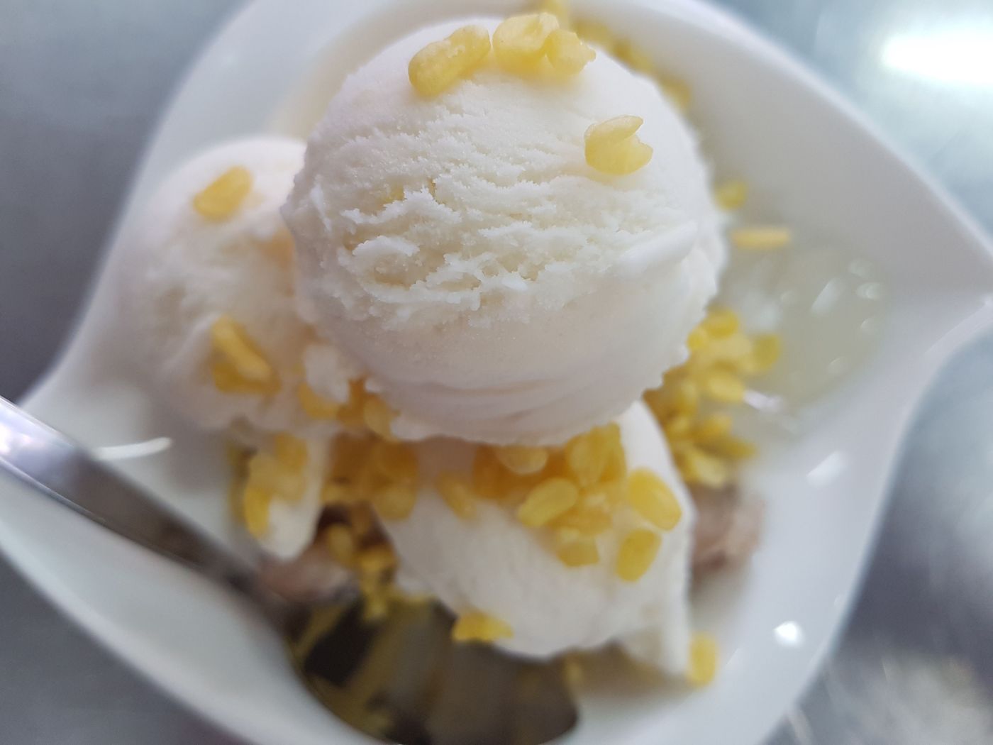 Two scoops of coconut ice cream on a plate, scattered with kernels of sweetcorn