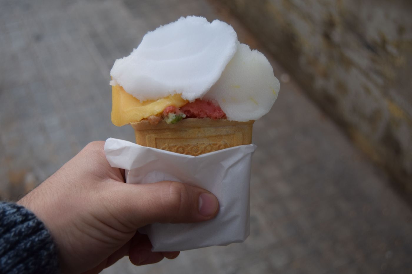 A cone of mixed ice cream, pale and pink, held in a paper napkin