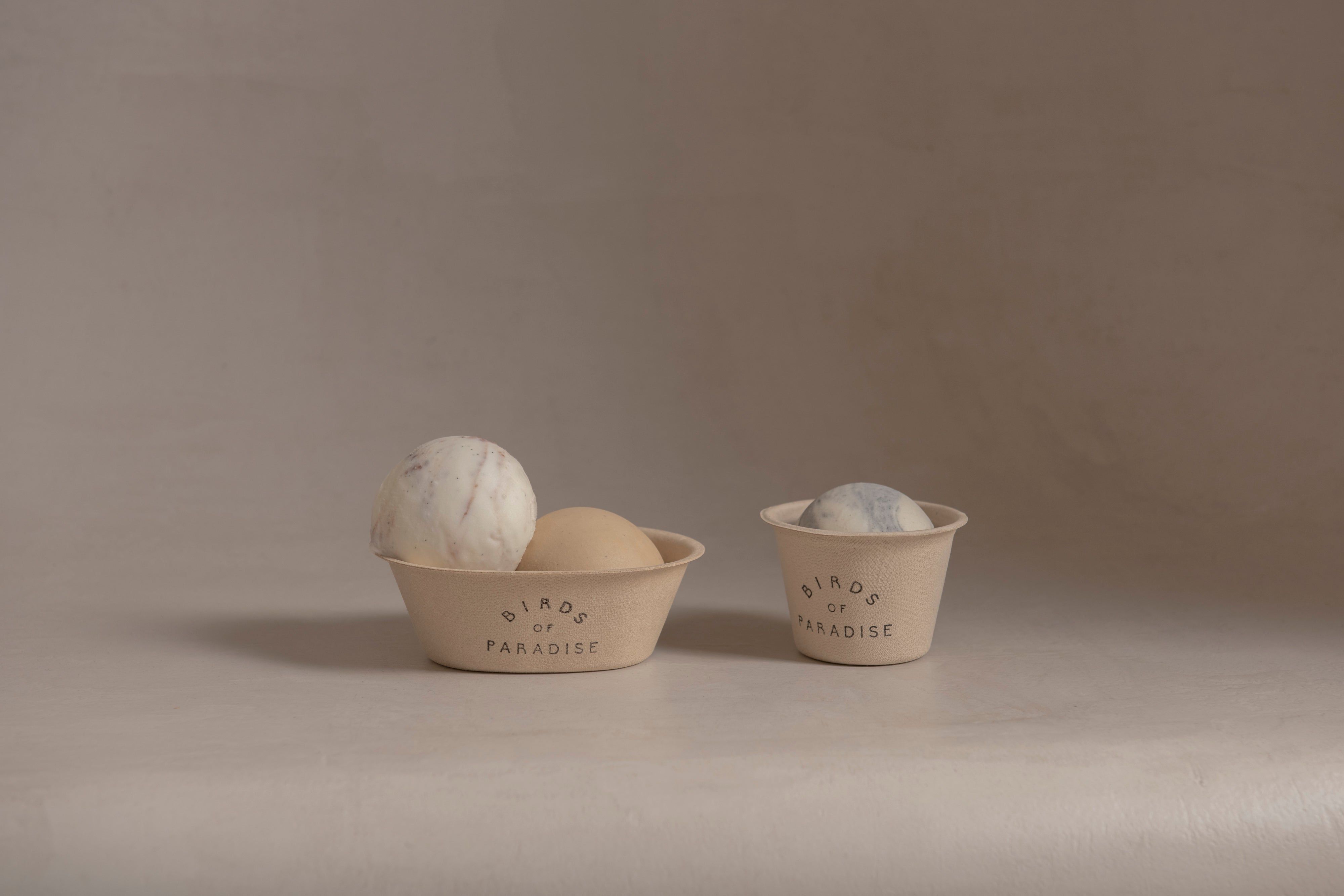 Two small stoneware cups, each holding a single pale scoop, on a bare beige surface