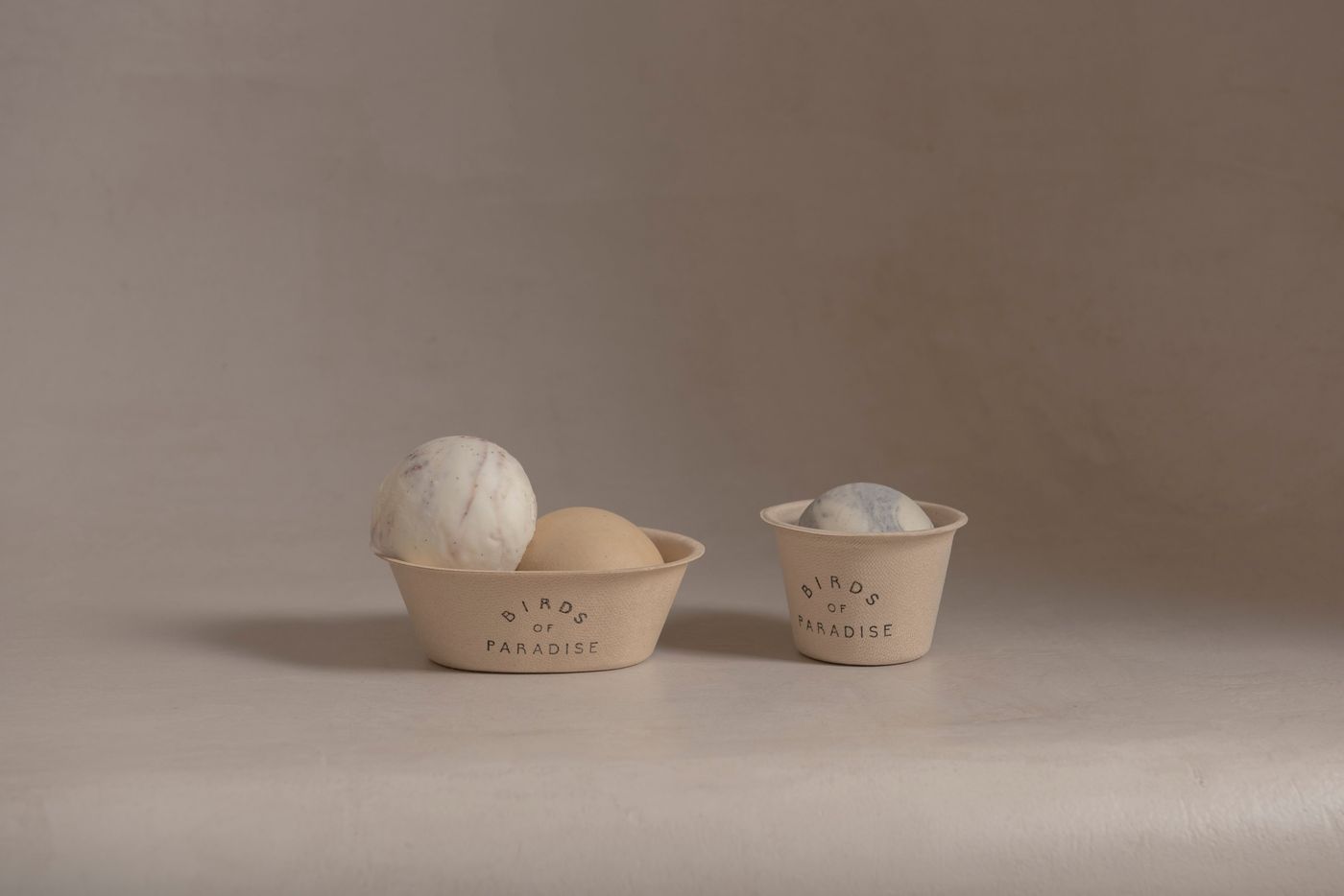Two small stoneware cups, each holding a single pale scoop, on a bare beige surface