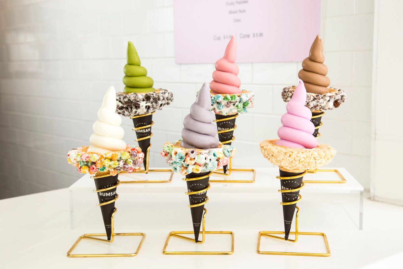 Four soft-serve cones in different colours, each rimmed with sprinkles and standing in its own gold wire holder