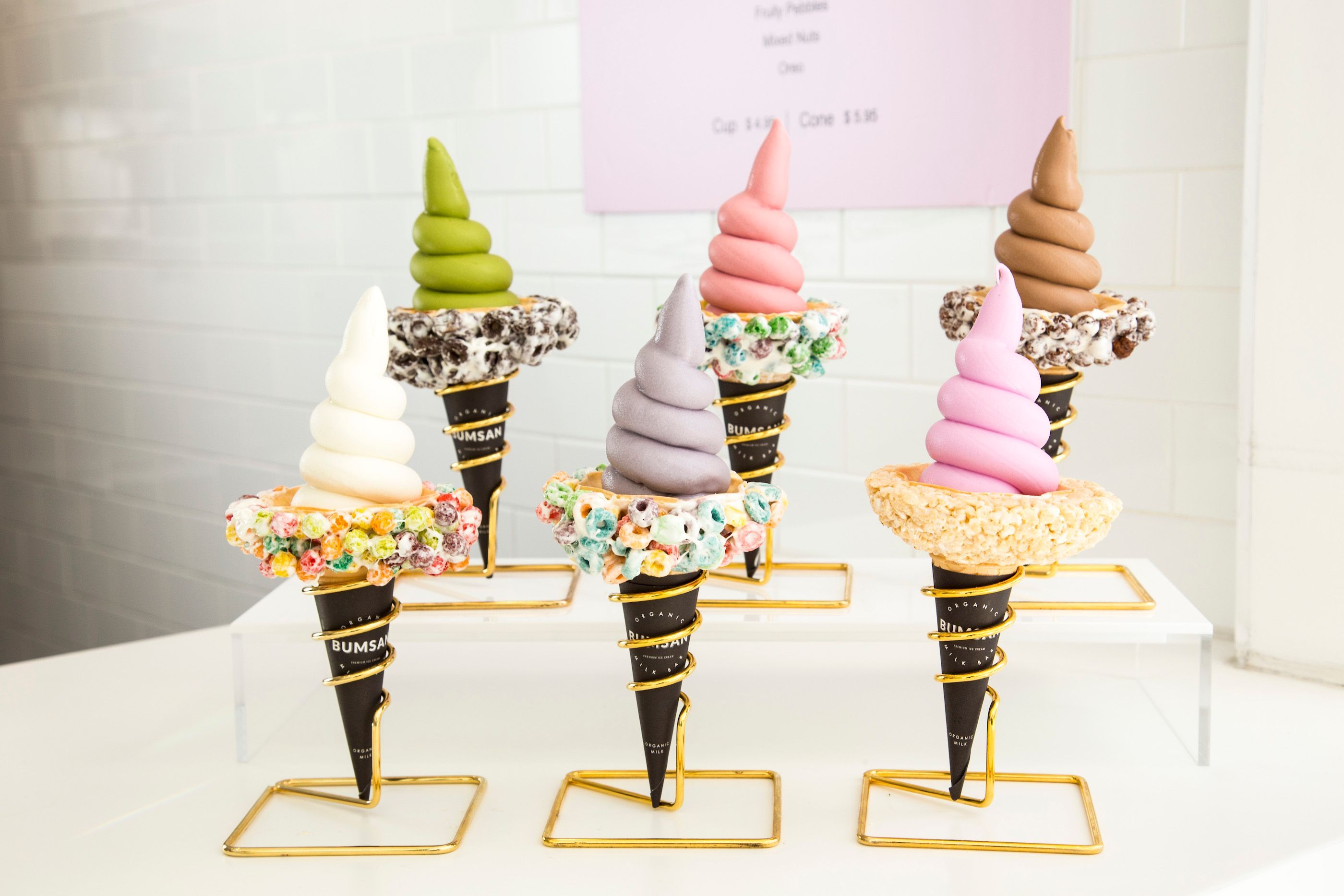 Four soft-serve cones in different colours, each rimmed with sprinkles and standing in its own gold wire holder