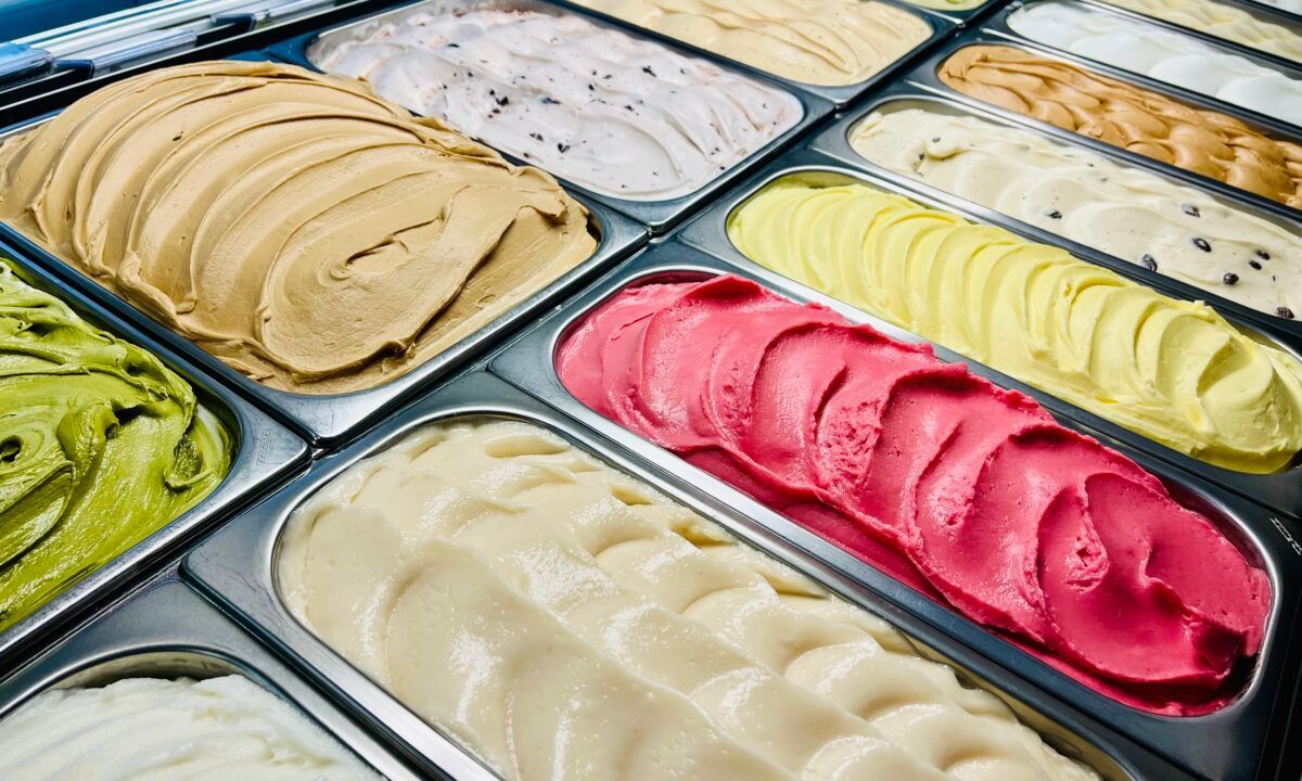 Rows of gelato in different colours and flavours in metal trays inside a chilled display case