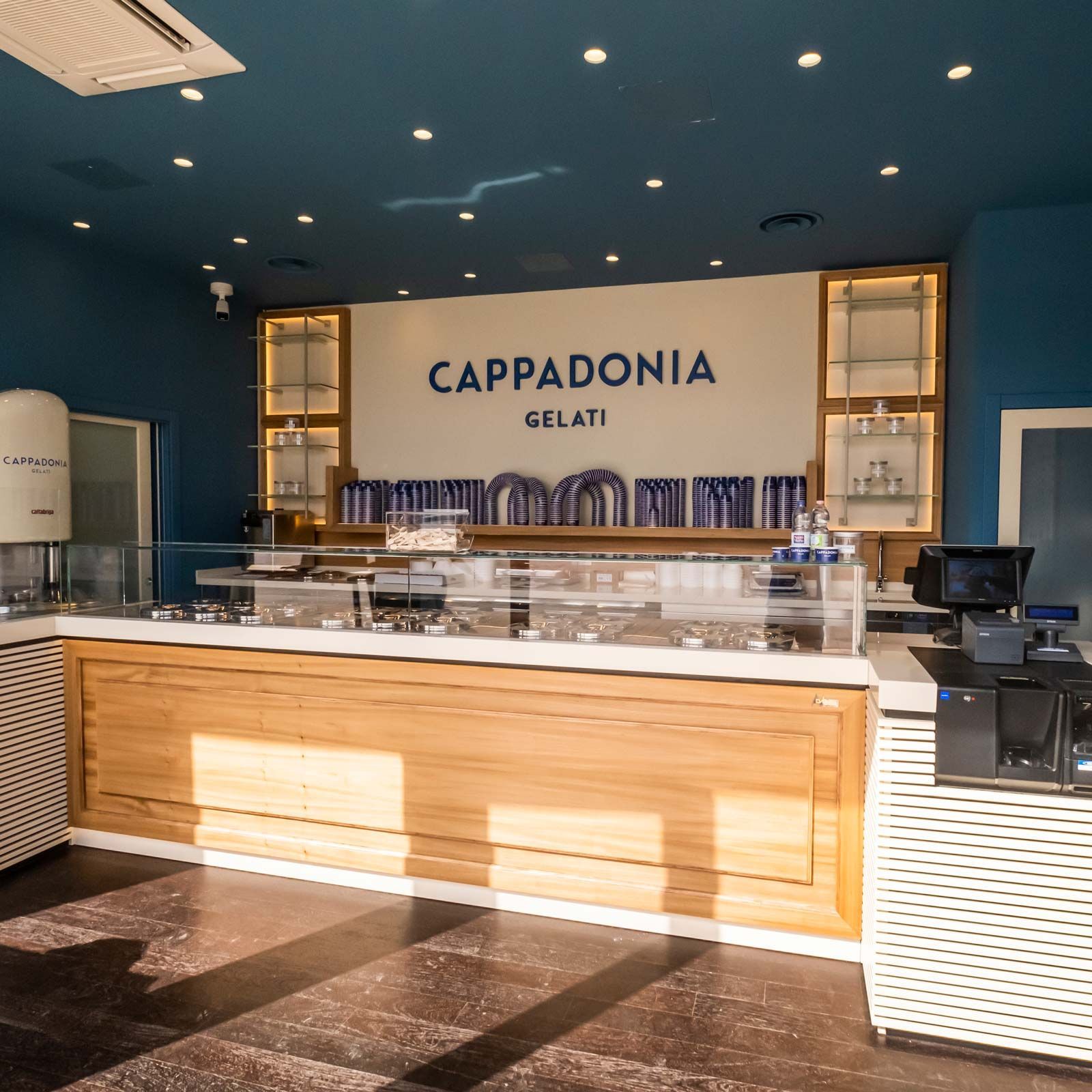 The counter and display case, pale wood against a deep blue wall under the Cappadonia Gelati sign