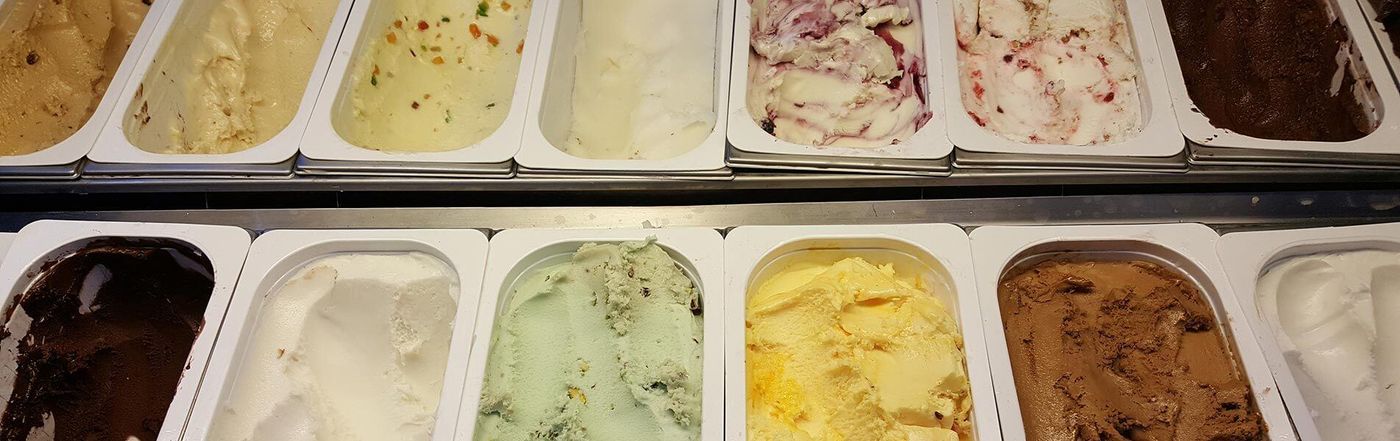 Two rows of ice-cream tubs in the display case, pale green pistachio, bright yellow and a berry-rippled white among them