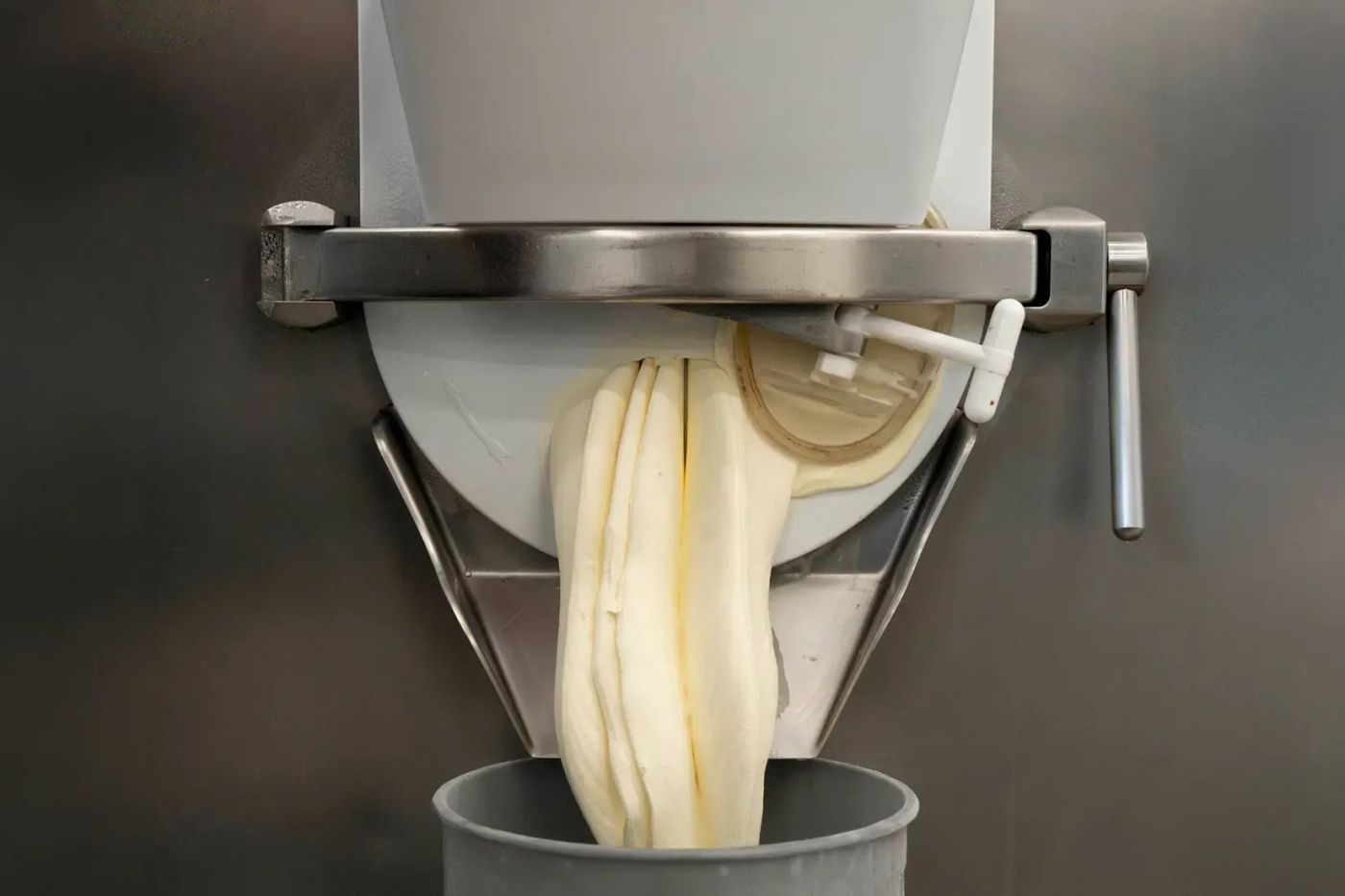 Pale gelato extruding in a thick ribbon from the spout of a batch freezer into a tub below