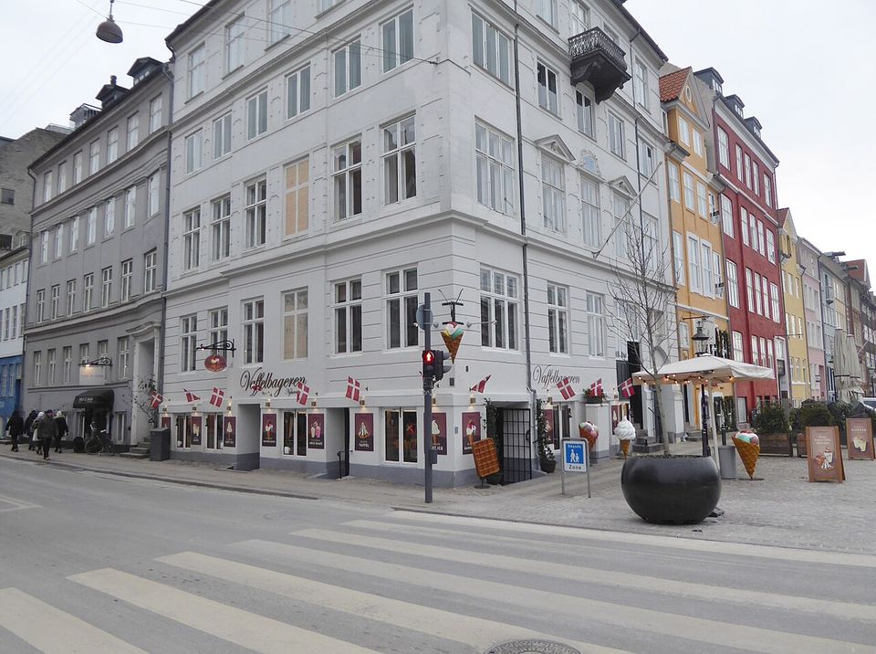 A corner ice-cream shop hung with a cone-shaped sign and small Danish flags, giant cone models standing on the pavement outside