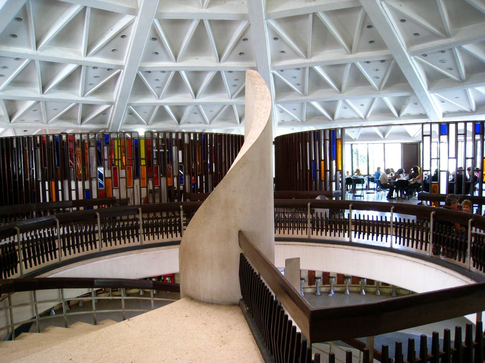 The interior of the Coppelia pavilion: a white latticed concrete canopy over curving ramps, stained-glass screens and tables of seated customers
