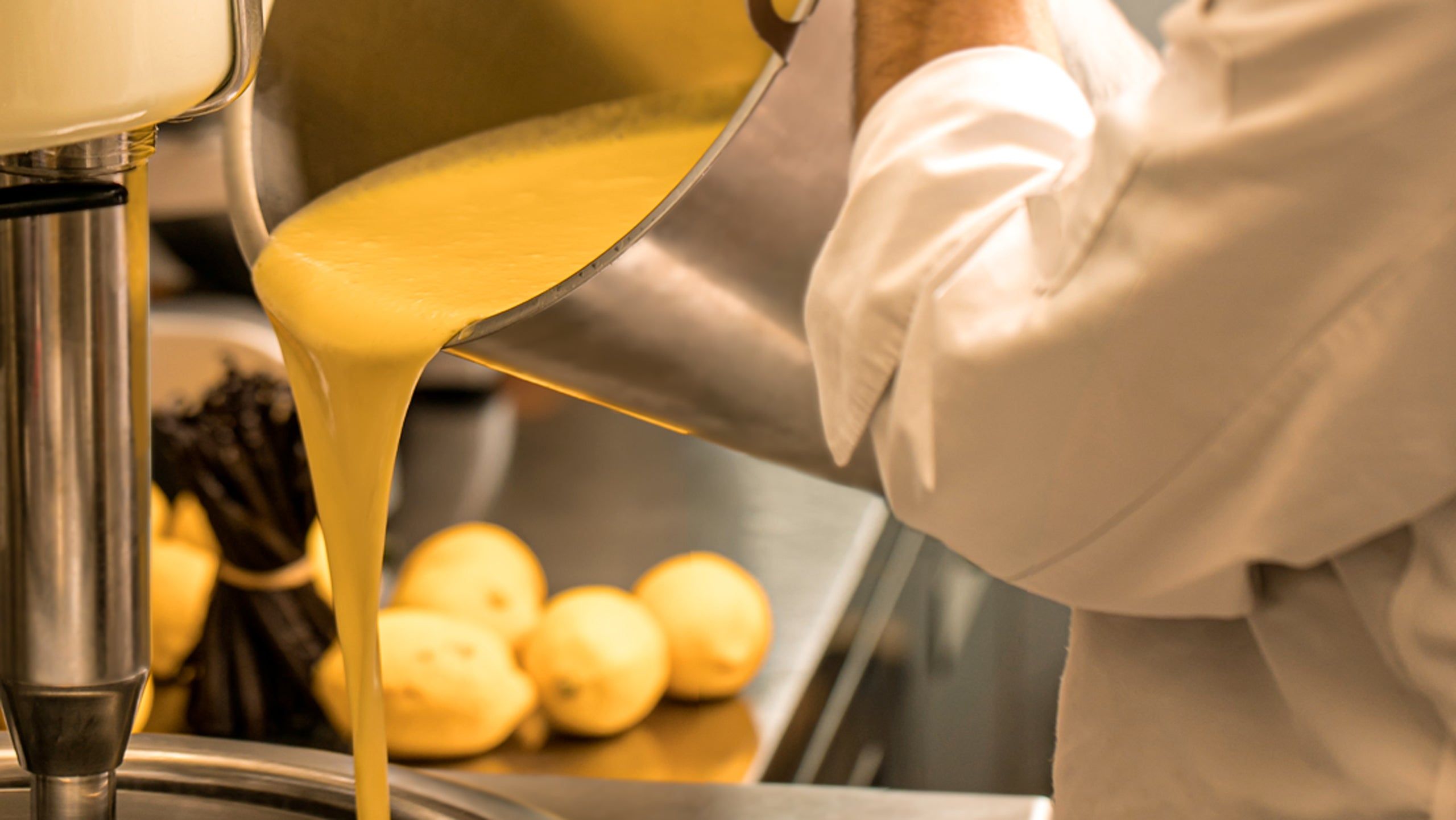 A maker in whites pouring a stream of yellow mix over rows of pale spheres