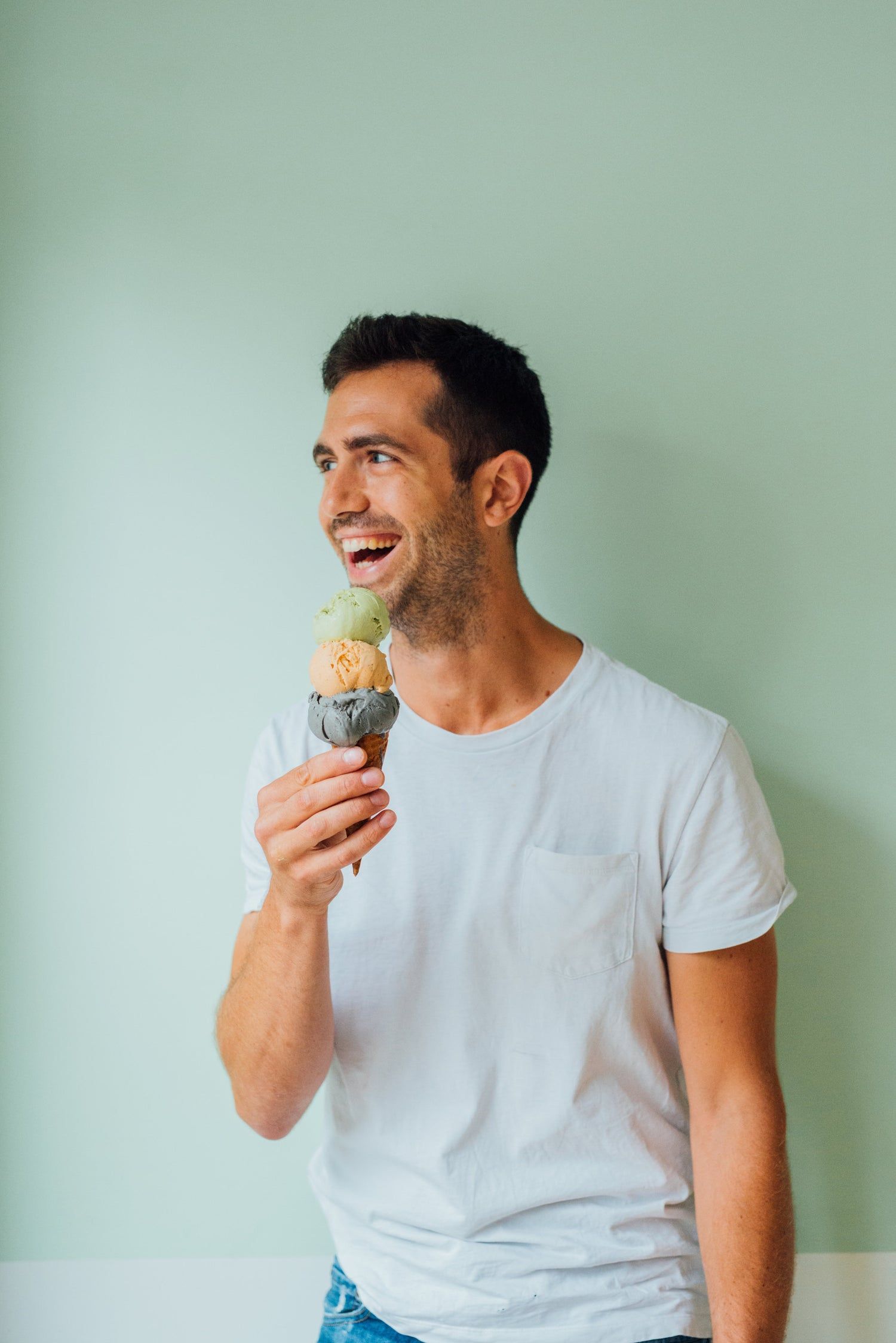 A man laughing, holding a cone of three scoops up beside his face