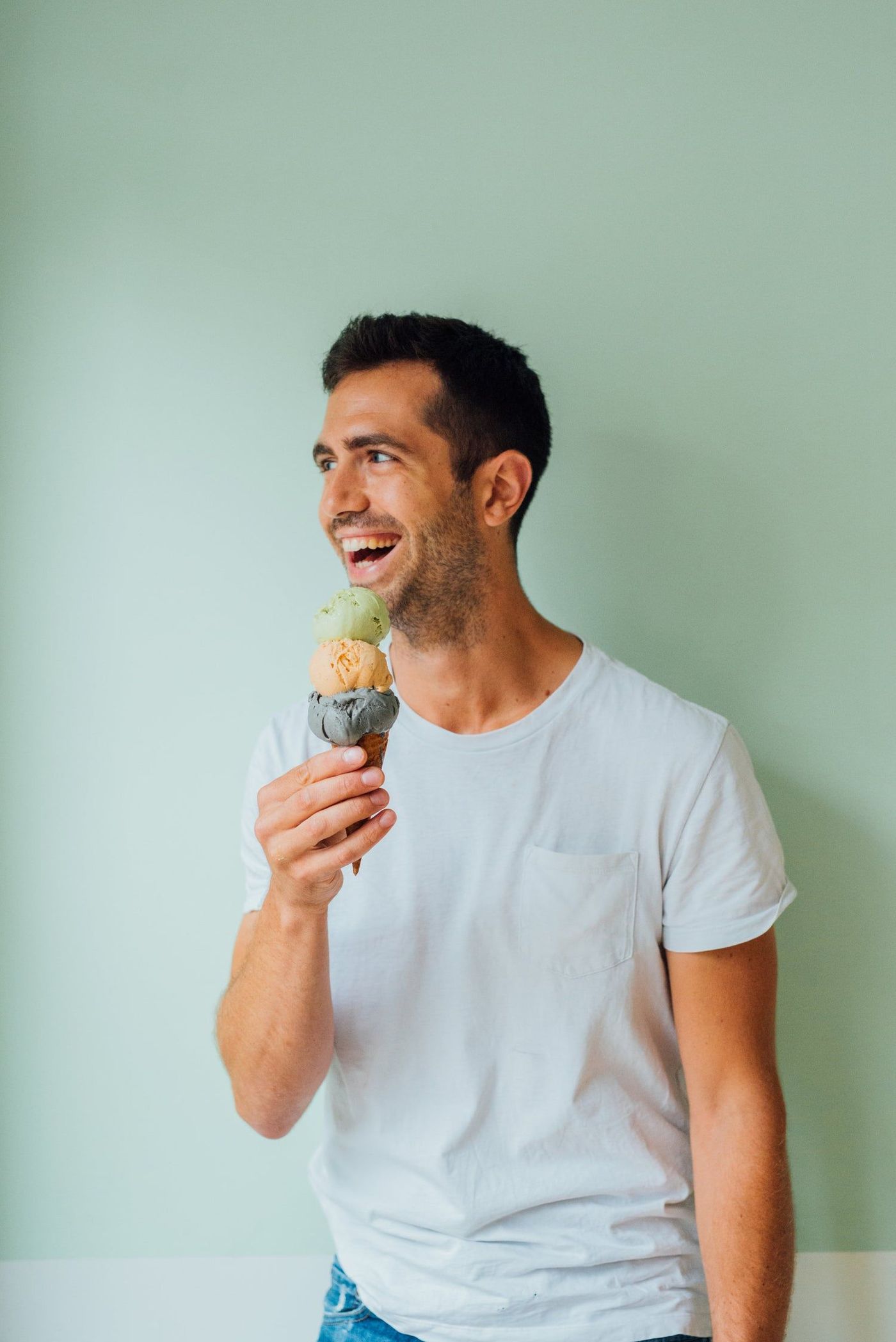 A man laughing, holding a cone of three scoops up beside his face