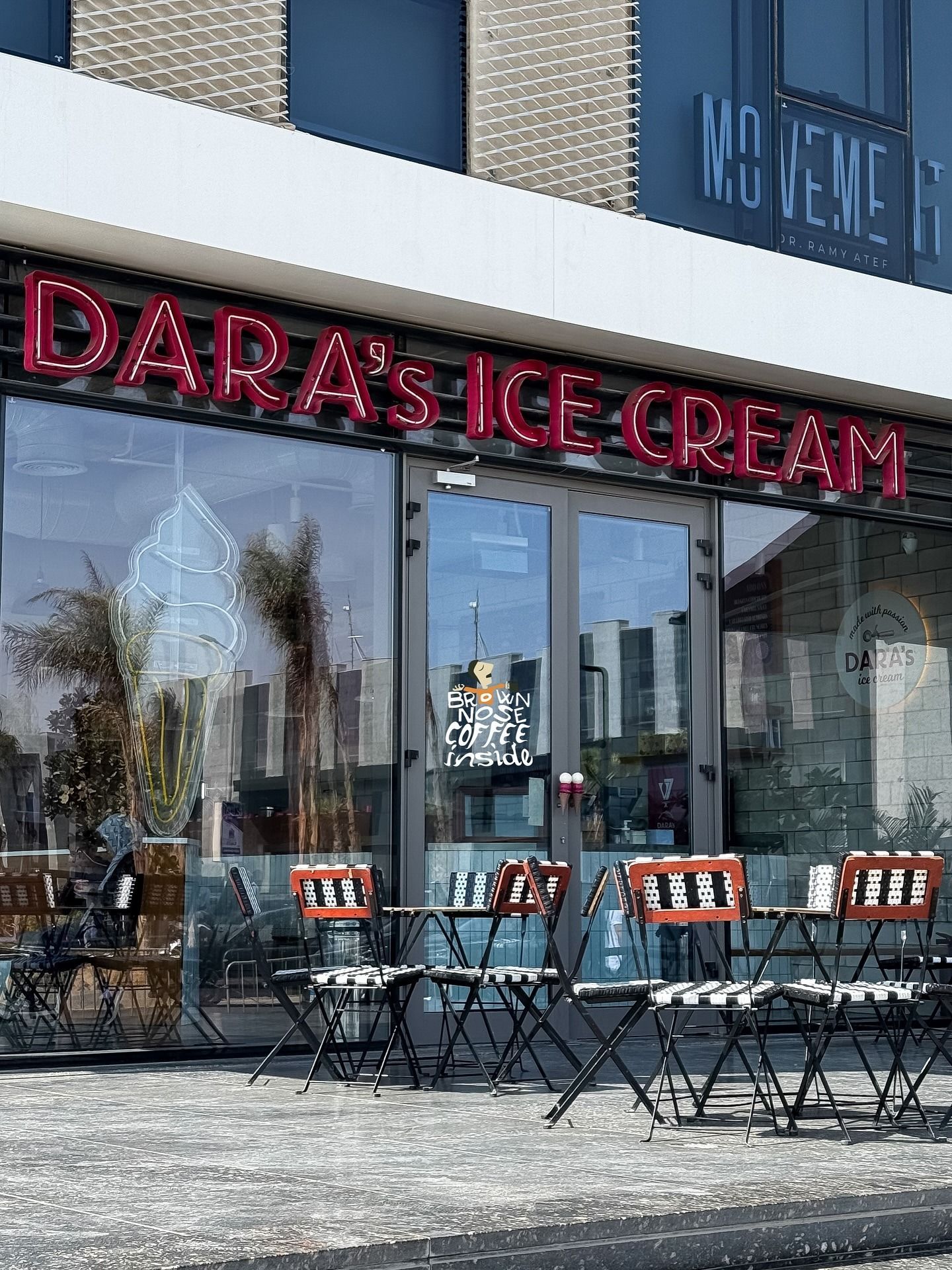 The shopfront at dusk under a pink neon DARA'S ICE CREAM sign, with chairs set out on the terrace