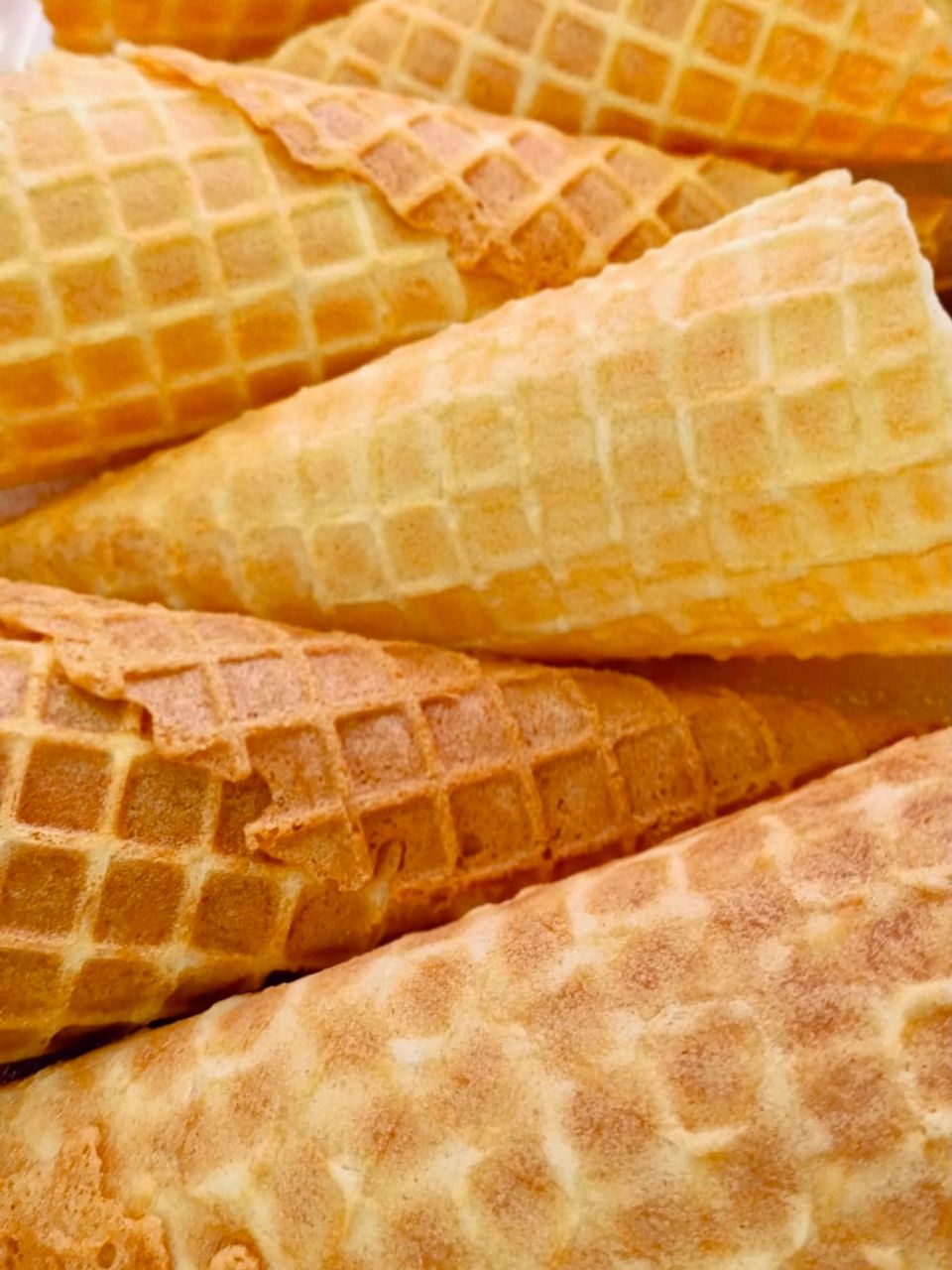 A close stack of golden waffle cones lying on their sides, their lattice pattern filling the frame