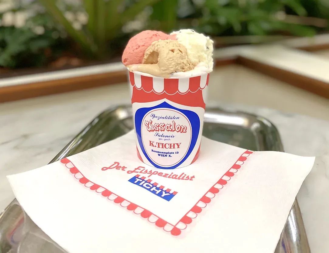 A cup of ice cream on a paper doily and a Tichy napkin, on a marble café table