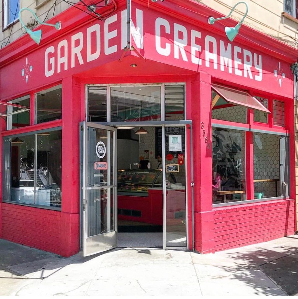 The red-painted corner shopfront with GARDEN CREAMERY lettered across the fascia, both glass doors propped open onto the sidewalk