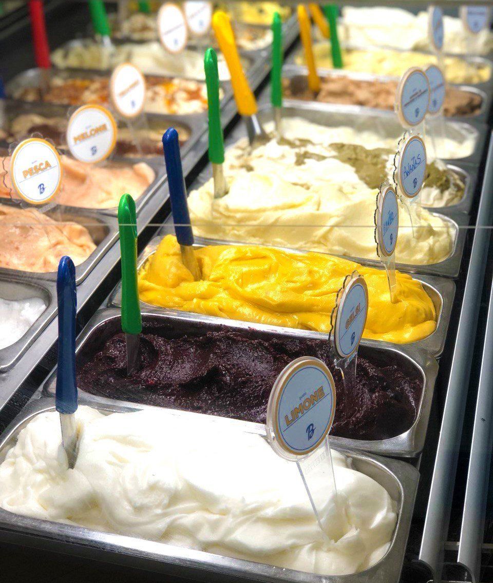 Stainless pans of gelato in the display case with coloured spades standing in them, the nearest cards reading Limone, Pesca and Melone
