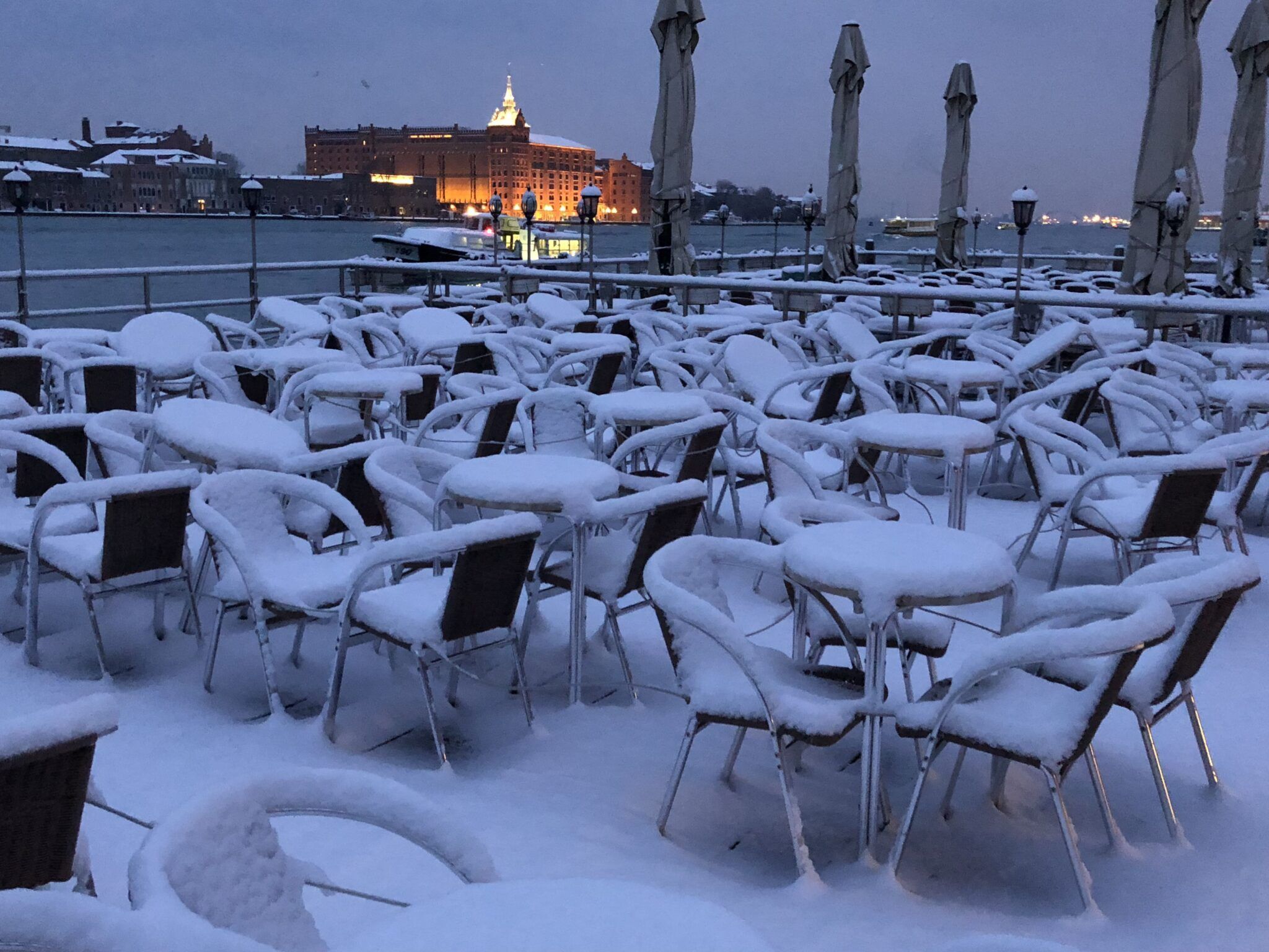 Café chairs and tables on the Zattere under snow, with San Giorgio Maggiore across the water