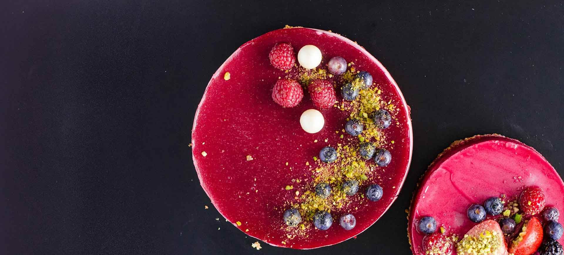A round tart glazed deep red and topped with raspberries, blueberries and small white spheres