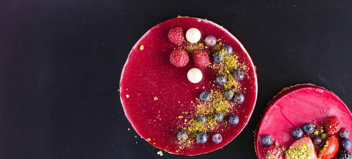 A round tart glazed deep red and topped with raspberries, blueberries and small white spheres
