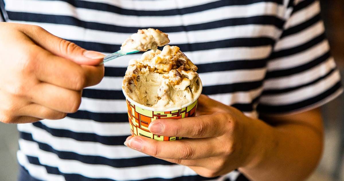 Hands in a striped shirt holding a tub of gelato with a spoon