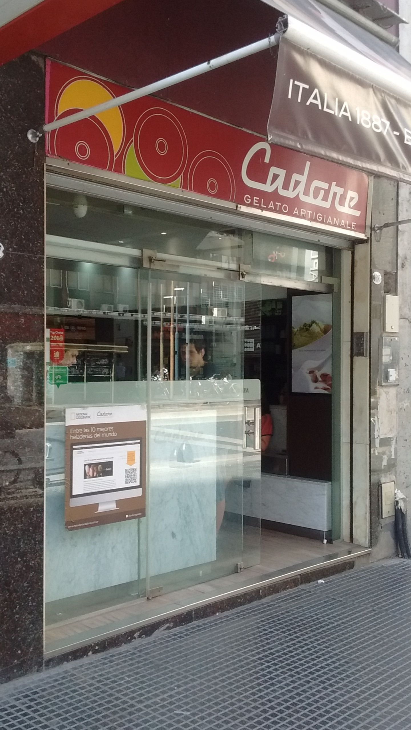 The Cadore shopfront on Avenida Corrientes: a red fascia reading Cadore Gelato Artigianale, an awning lettered ITALIA 1887, and a poster in the window naming it among the world's ten best heladerías