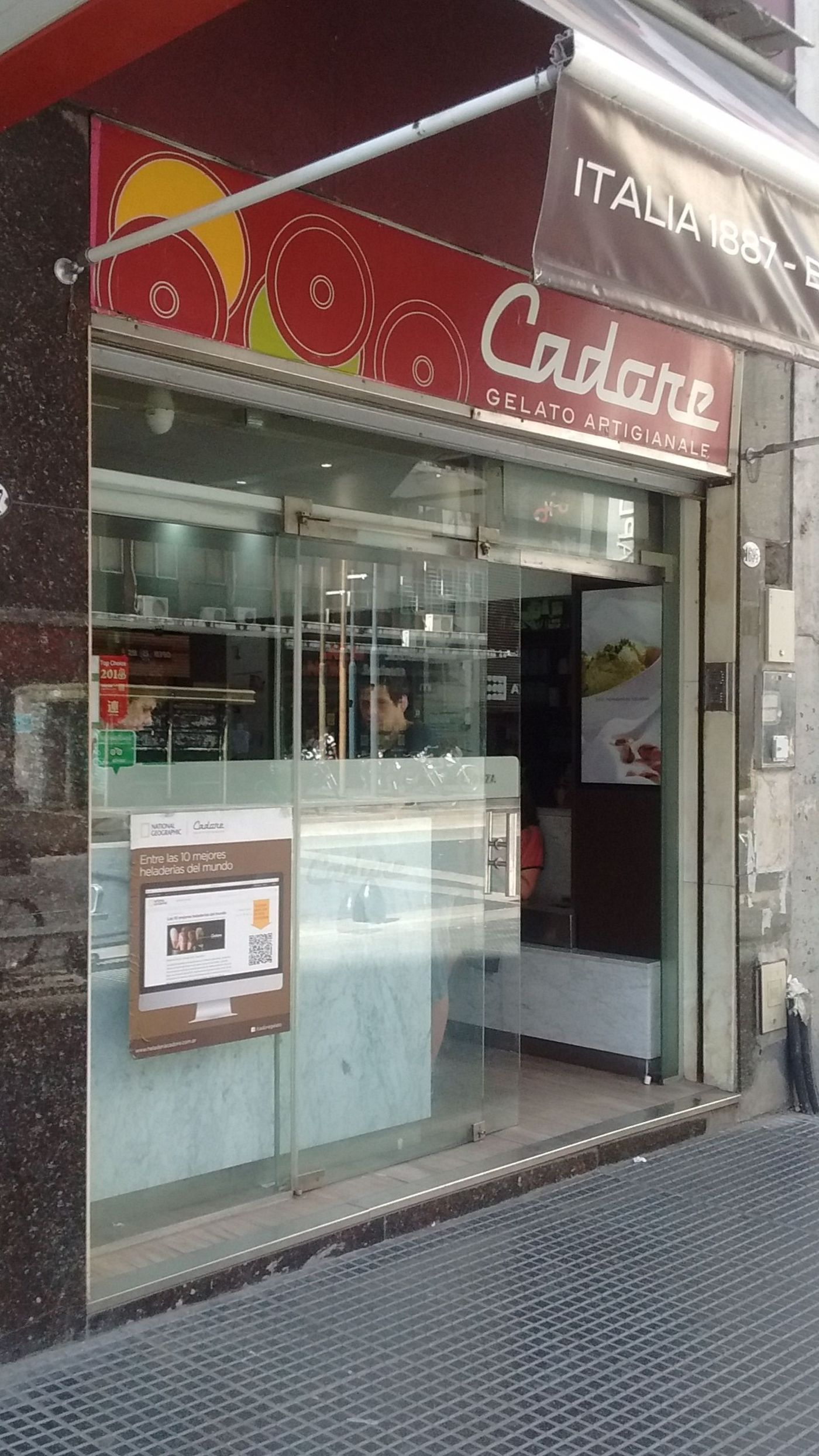 The Cadore shopfront on Avenida Corrientes: a red fascia reading Cadore Gelato Artigianale, an awning lettered ITALIA 1887, and a poster in the window naming it among the world's ten best heladerías