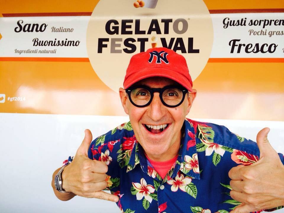 The maker in a red cap and a flowered shirt, both thumbs up, in front of a Gelato Festival banner