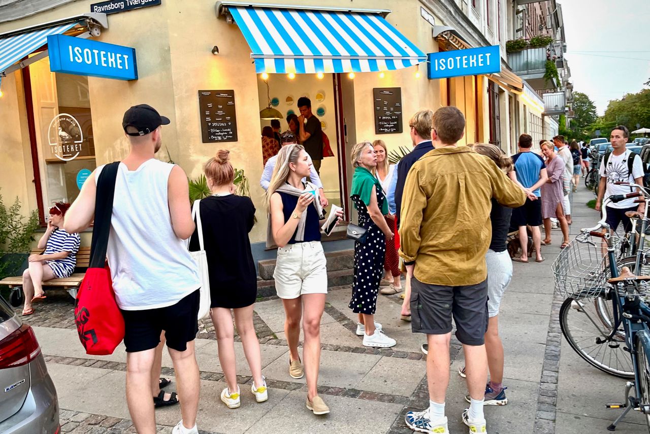 People queueing on the pavement outside the shop under striped awnings