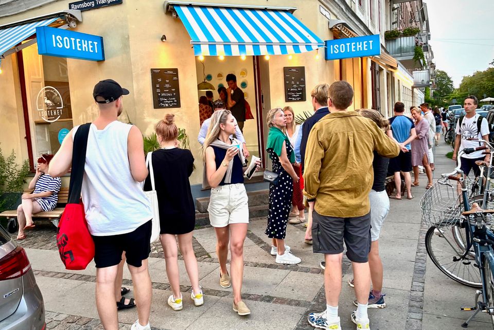 People queueing on the pavement outside the shop under striped awnings