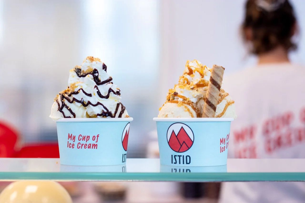 Two branded cups of soft serve, one dipped in chocolate, one with caramel and nuts