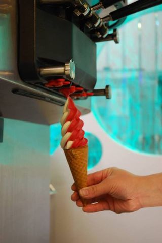 A red and white soft-serve swirl being drawn from the machine into a cone