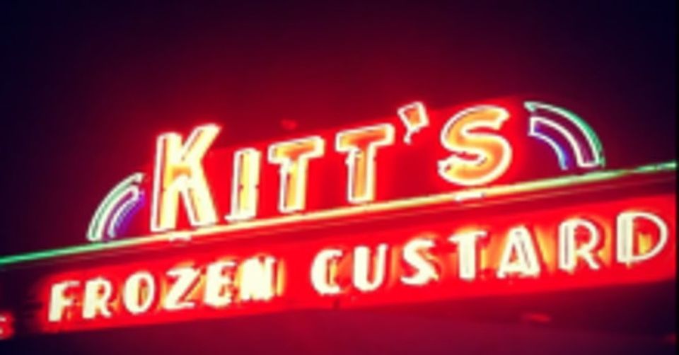 A red neon sign reading Kitt's Frozen Custard lit against a dark night sky, with a small neon rainbow arc at each end