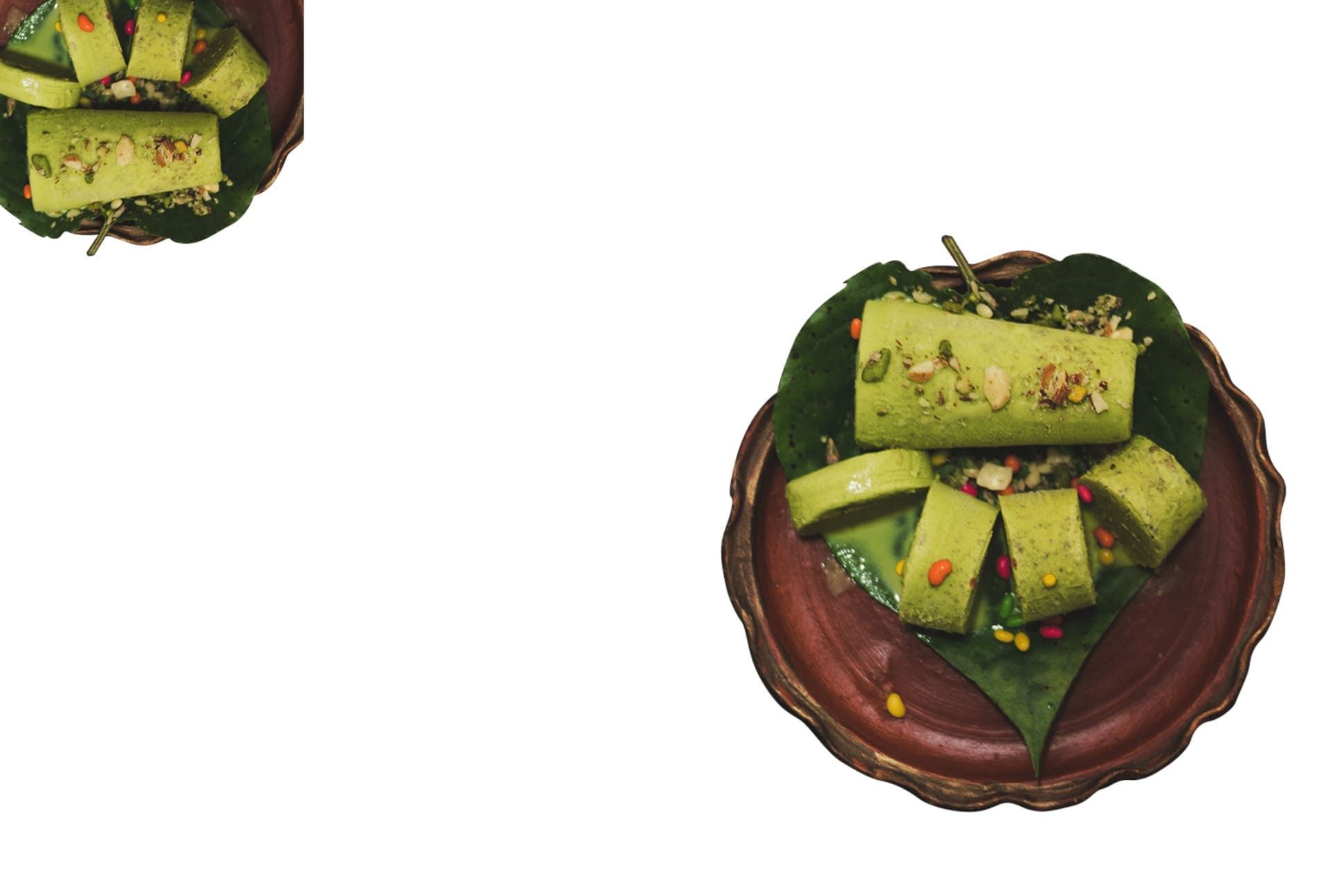 Slices of pistachio kulfi on a wooden dish beside dark red fruit kulfi arranged on a black plate