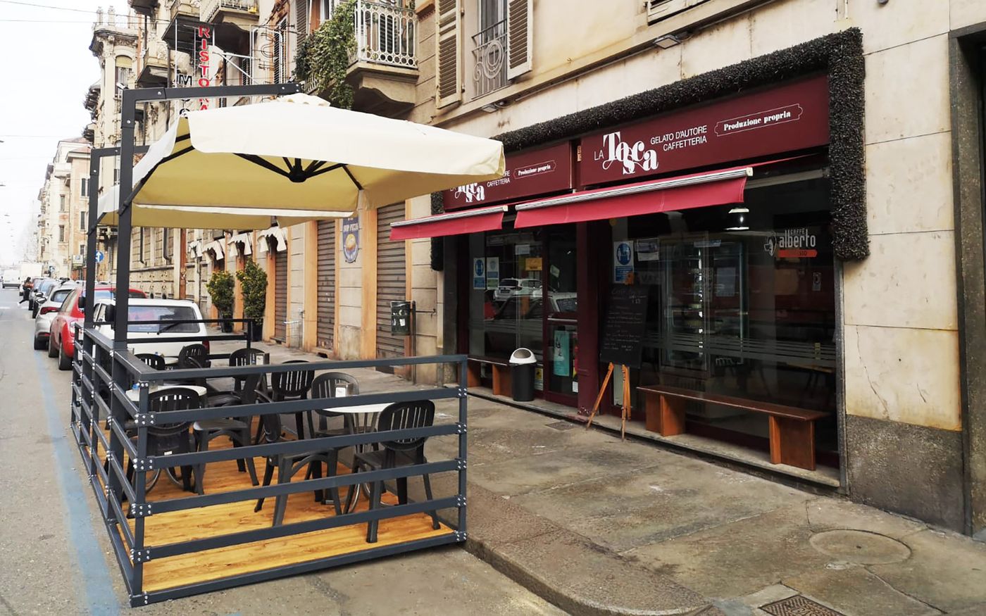 The shop's burgundy frontage on a Turin street, signed La Tosca — gelato d'autore, caffetteria, produzione propria, with an empty fenced pavement terrace of tables, chairs and a cream parasol beside it