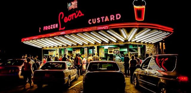 The neon-lit drive-in at night, cars pulled up under the Leon's Frozen Custard sign