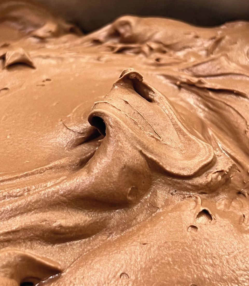 A close-up of chocolate gelato in a tray, its surface drawn into ridges by the spatula