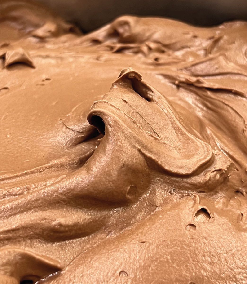 A close-up of chocolate gelato in a tray, its surface drawn into ridges by the spatula