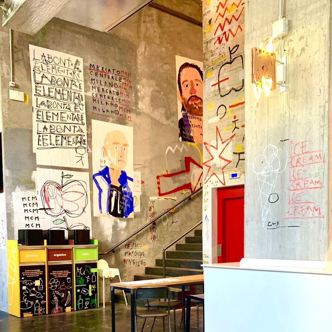 Tubs stacked outside a doorway on a Milan street, the wall behind covered in painted lettering and murals
