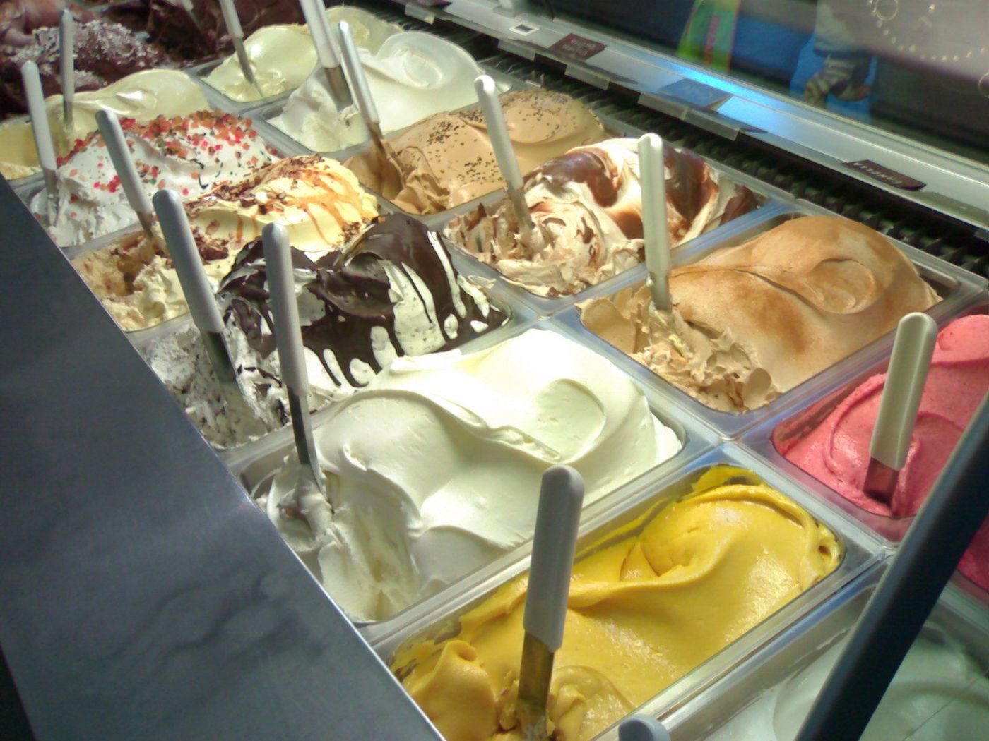 A chilled case packed with trays of gelato, a scoop standing in each