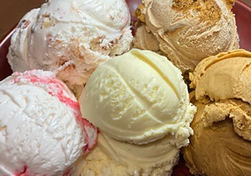 A close crop of scoops packed together in a display case, pale green, pink, cream and coffee