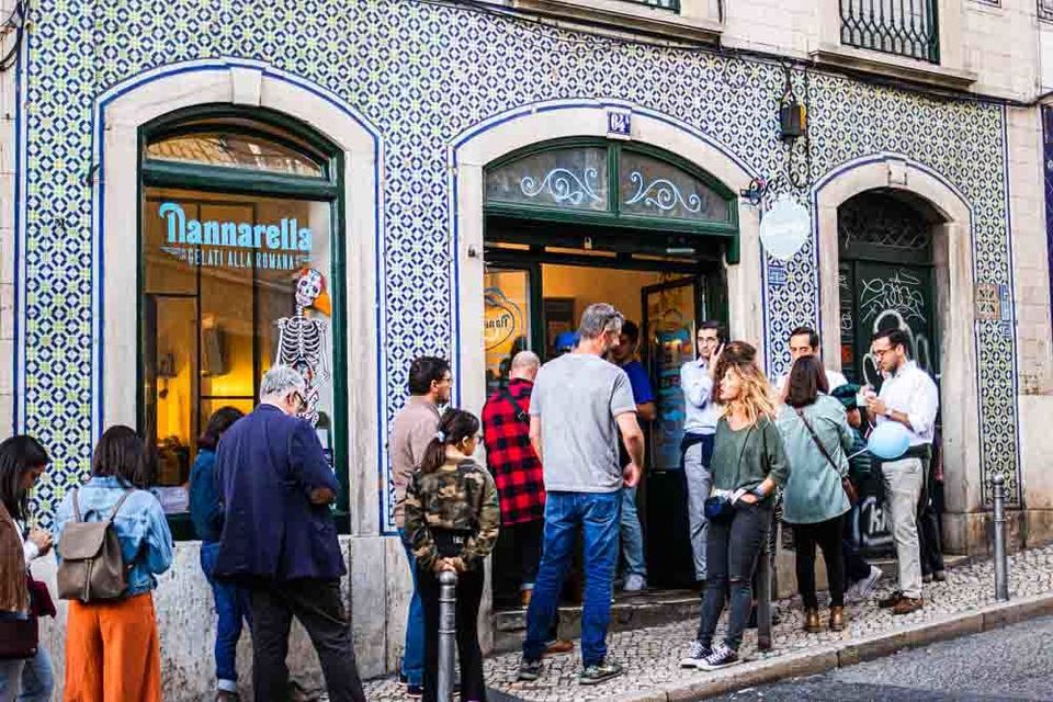A crowd waits on the pavement outside a blue-and-white azulejo-tiled frontage whose window is lettered Nannarella — gelati alla romana, with the door standing open beside it