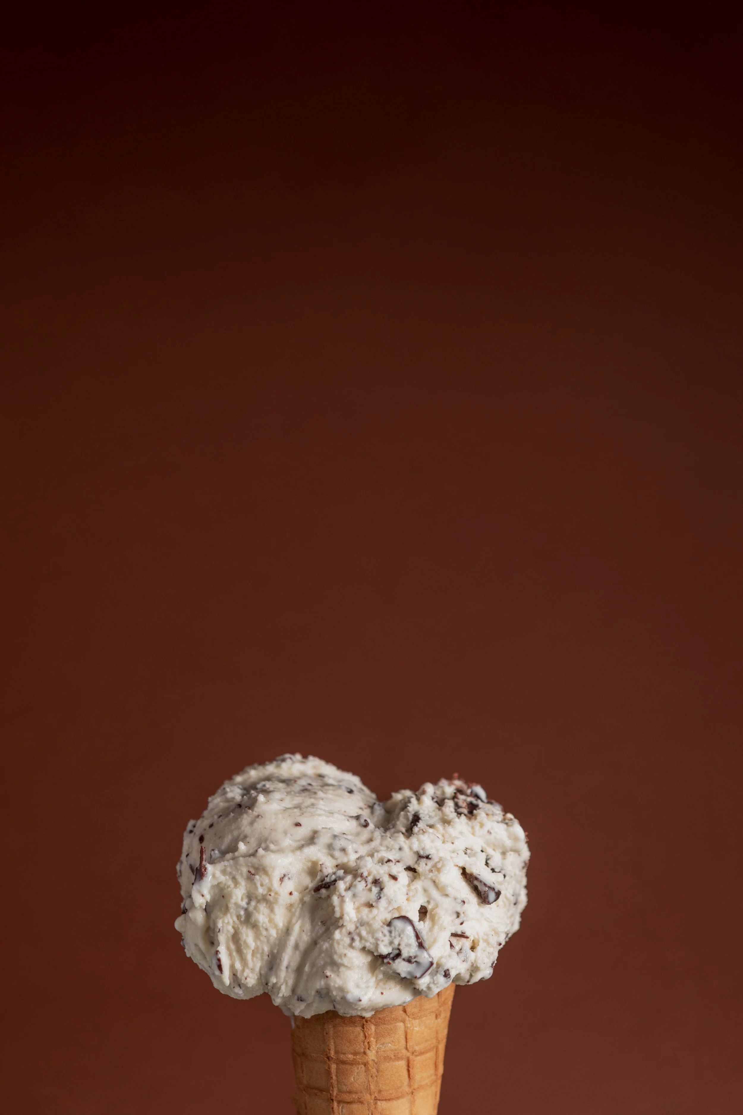 A single scoop on a cone against a deep red-brown ground