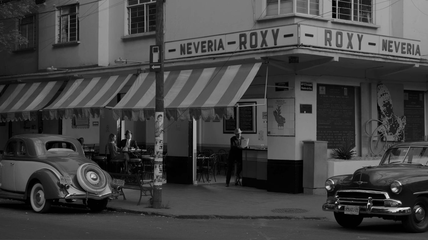 An archive black-and-white photograph of the Roxy shopfront with period cars at the kerb
