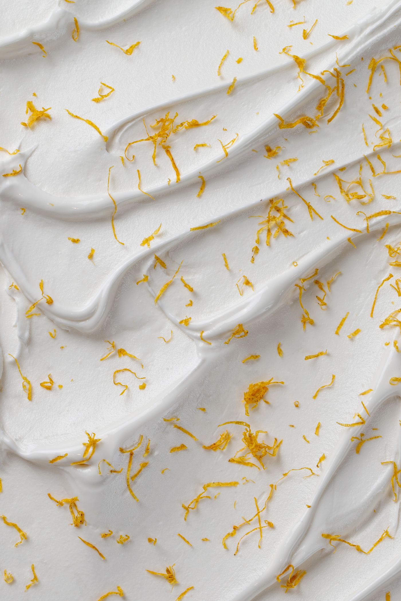 An extreme close-up of the swirled surface of white ice cream scattered with fine strands of yellow citrus zest