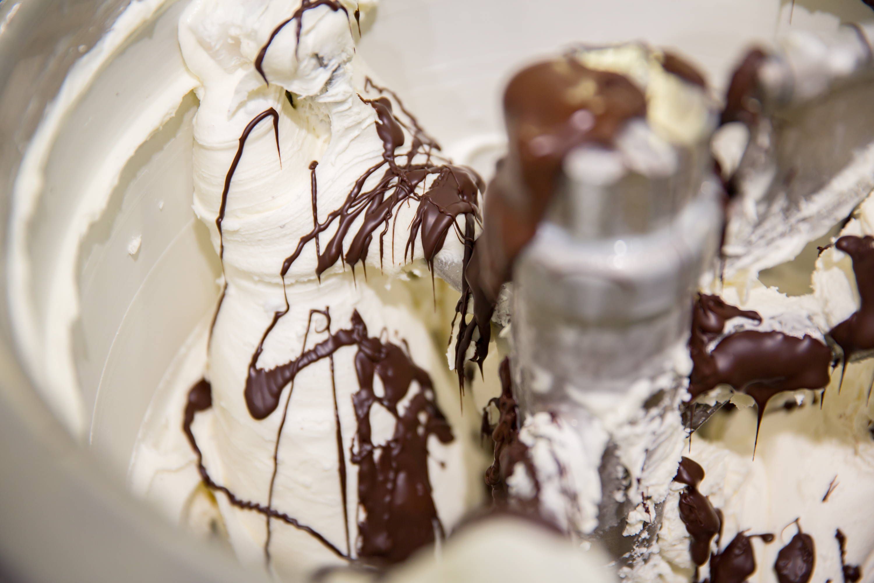 Chocolate sauce poured over whipped cream, photographed close enough that the pour fills the frame