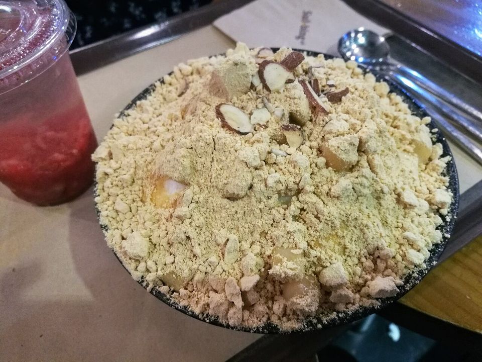 A mound of shaved ice buried under roasted soybean powder and sliced almonds, a red slush drink beside it on the tray