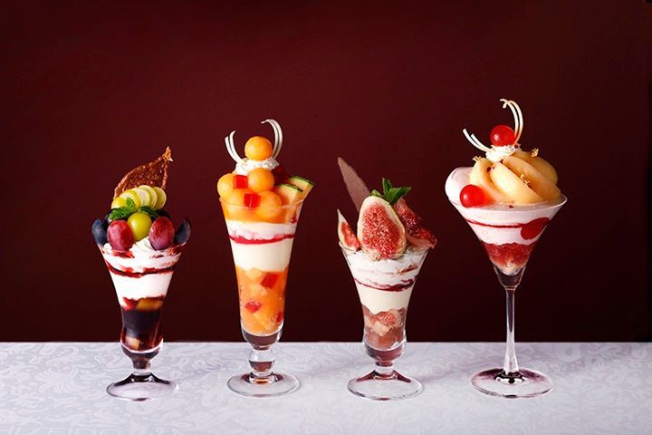 Four tall parfait glasses in a row, each layered differently with fruit and cream
