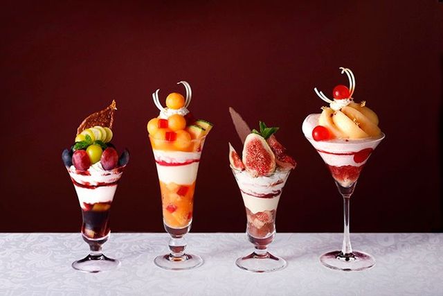 Four tall parfait glasses in a row, each layered differently with fruit and cream