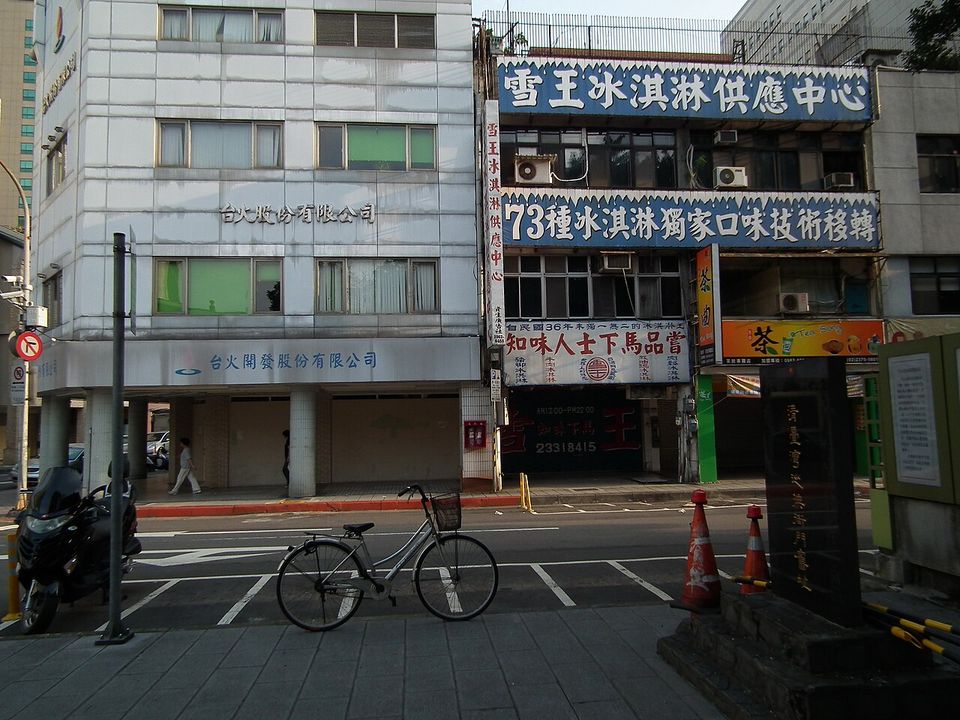 Blue and white boards stacked up a narrow shopfront advertising ice cream in 73 flavours, a bicycle parked at the kerb opposite